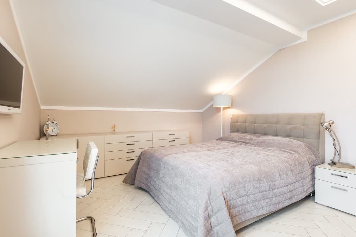 A bright, tidy small bedroom with a desk, drawers and a made bed