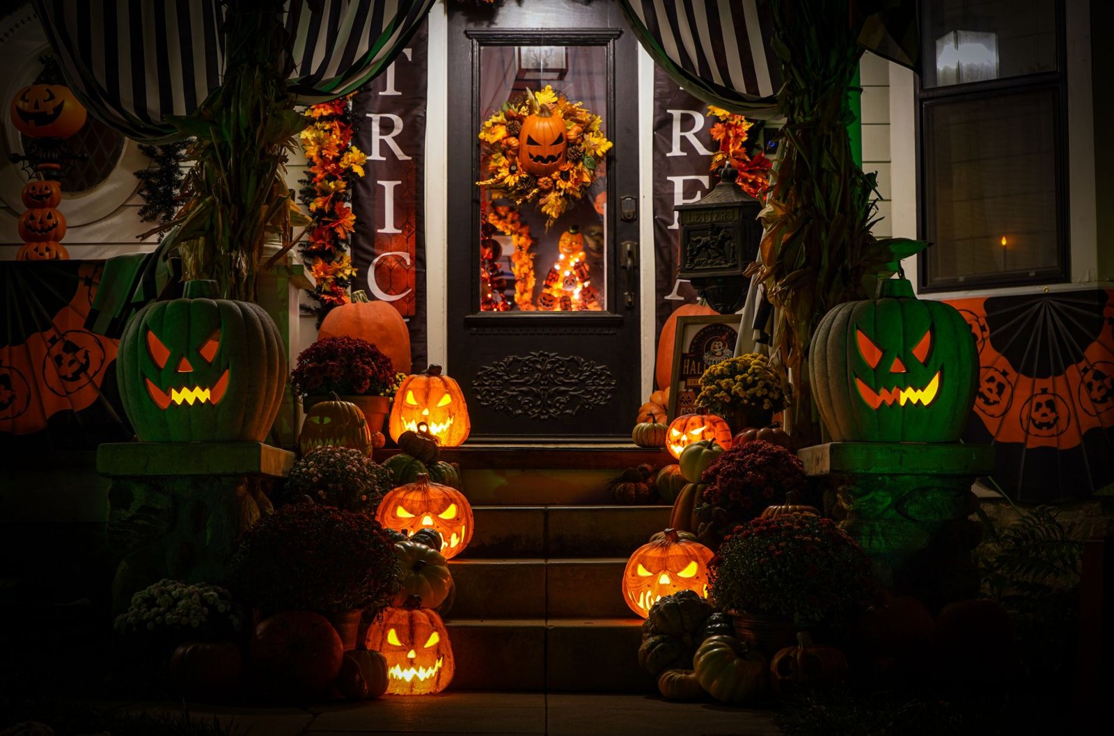 A suburban porch decorated with glowing pumpkins and mums at dusk